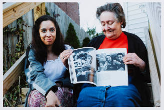 Color photo of a young woman and older woman holding a book open to show black-and-white photos