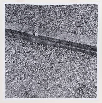Black-and-white square photo of a curb with rocks spilling over the curb stopper onto asphalt