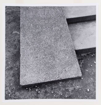 Close-up photograph of an upwardly sloped cement slab lying between cement stairs and ground
