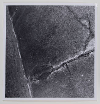 Close-up, square, black-and-white photograph of a cracked sidewalk meeting a cement wall