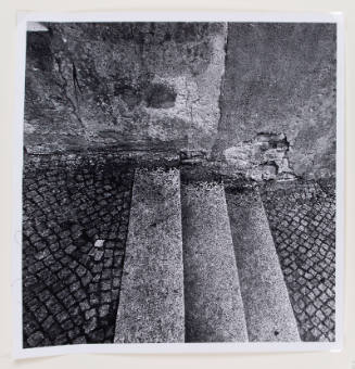 Close-up, black-and-white photograph of three stairs bridging tiled paths along a crumbling wall