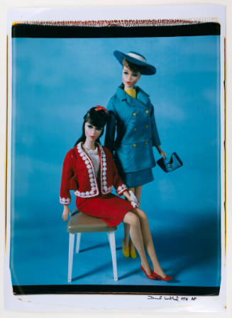 Color photo of two light-skinned Barbie dolls in skirts and blazers on blue background
