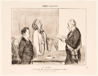 A man wearing a sash reads from a paper as a tall woman and a shorter man in a suit stand before him