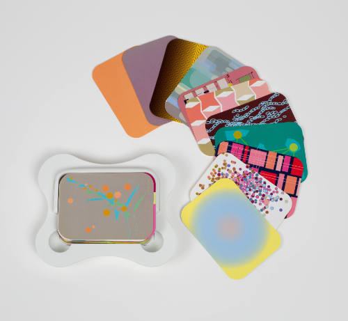 Curved white plastic case holds deck of cards with bright patterns, with some displayed at right