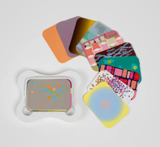 Curved white plastic case holds deck of cards with bright patterns, with some displayed at right